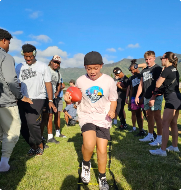 A young boy is holding a football in front of a group of people.