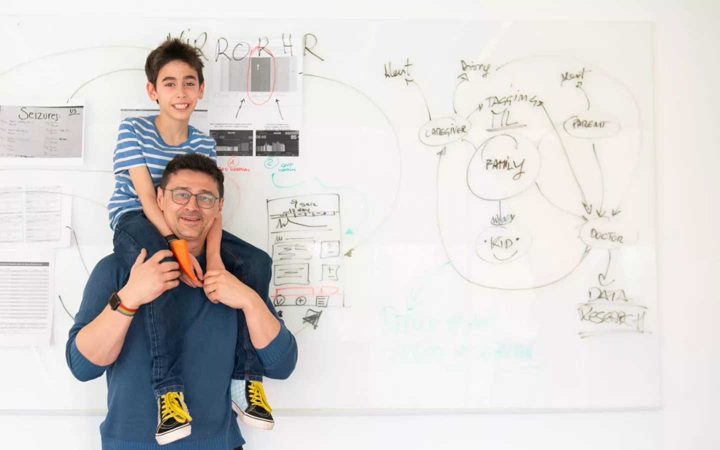 A man holding his son in front of a whiteboard.