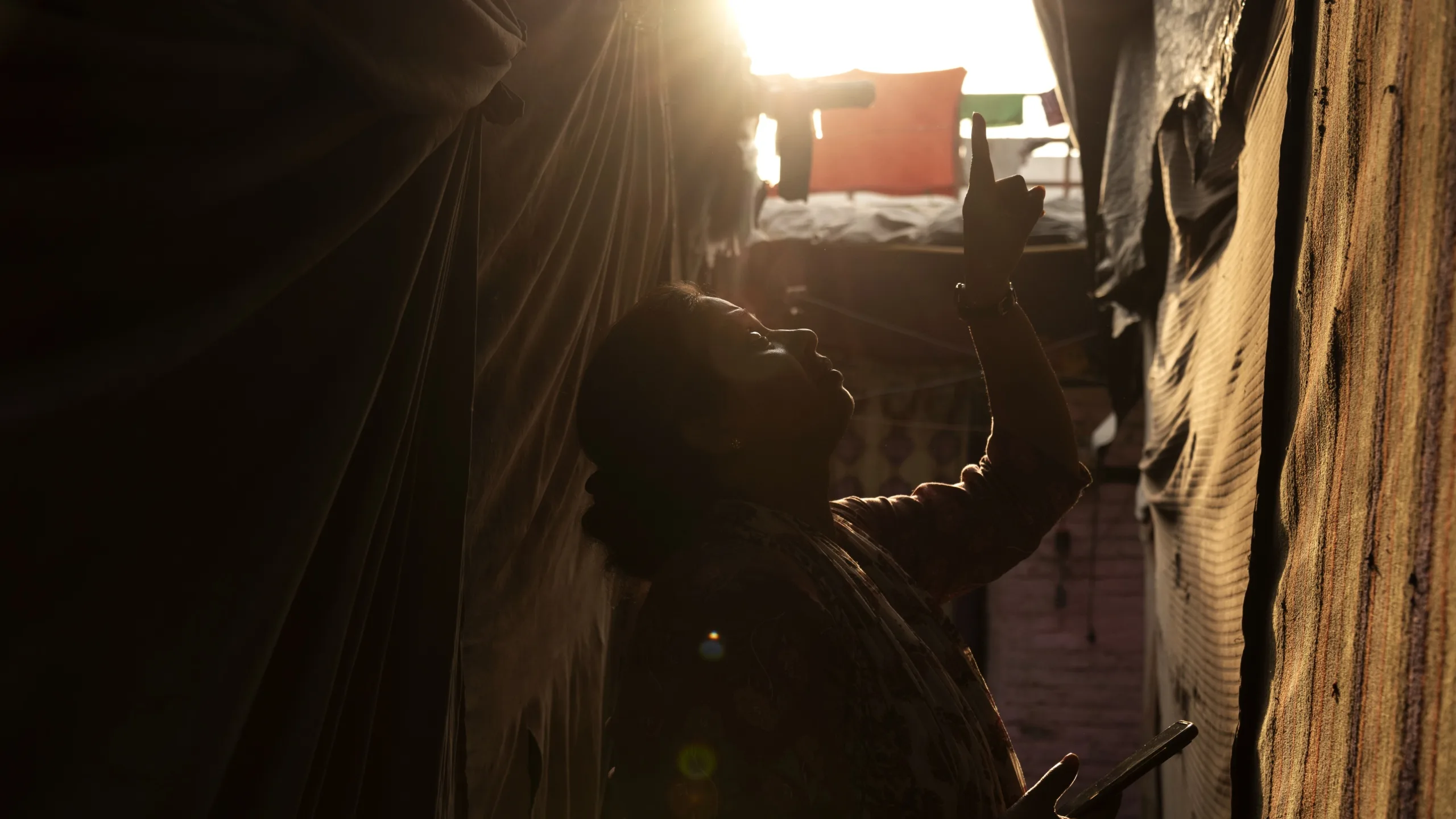 A woman stands outside of a home in a densely packed neighborhood and points to its roof.