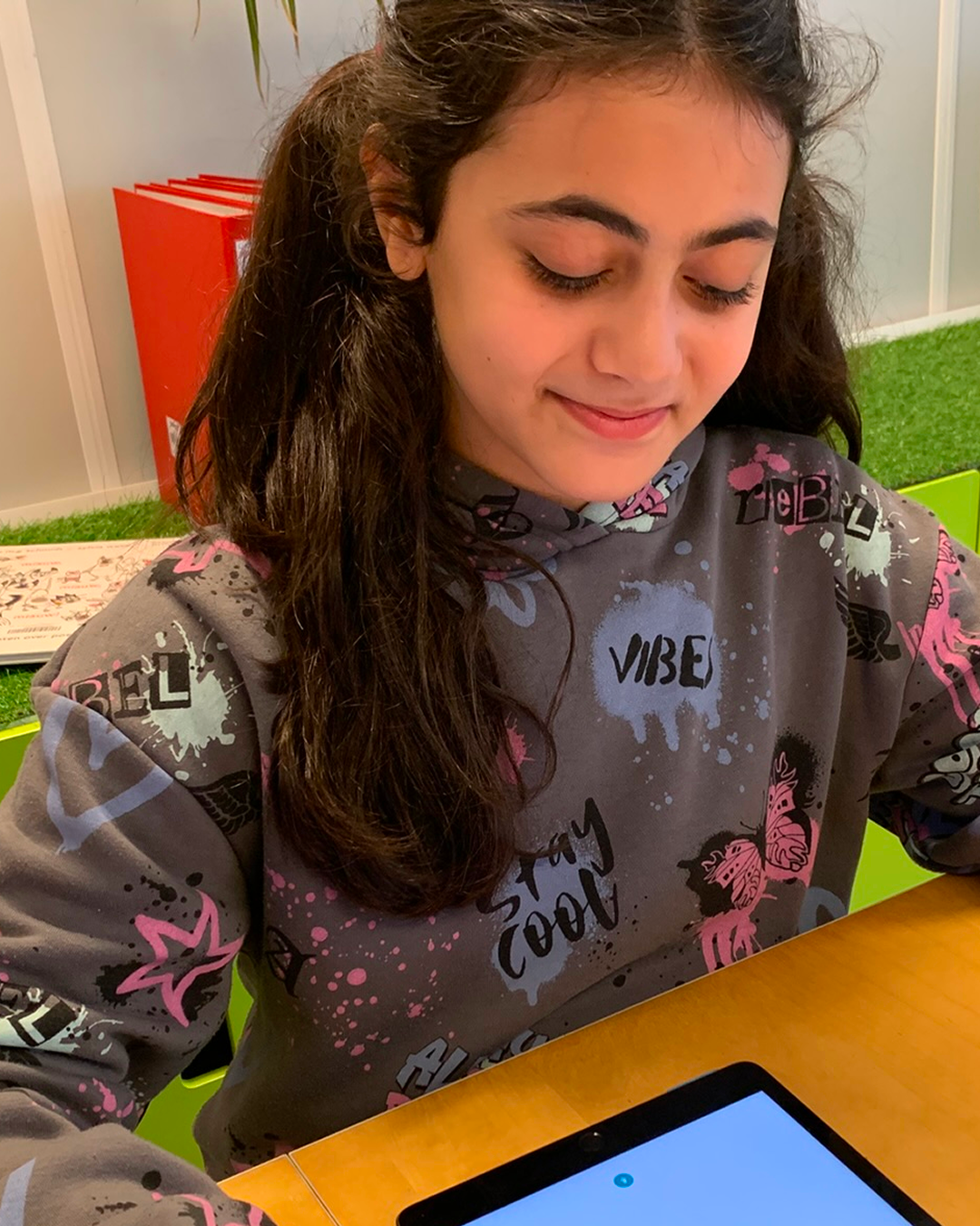 A girl wearing a colorful hoodie with graffiti-style designs using a tablet