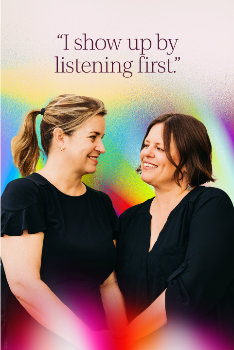 Two women stand facing each other, smiling and holding hands, with a colorful background and the text, "I show up by listening first." displayed above them.